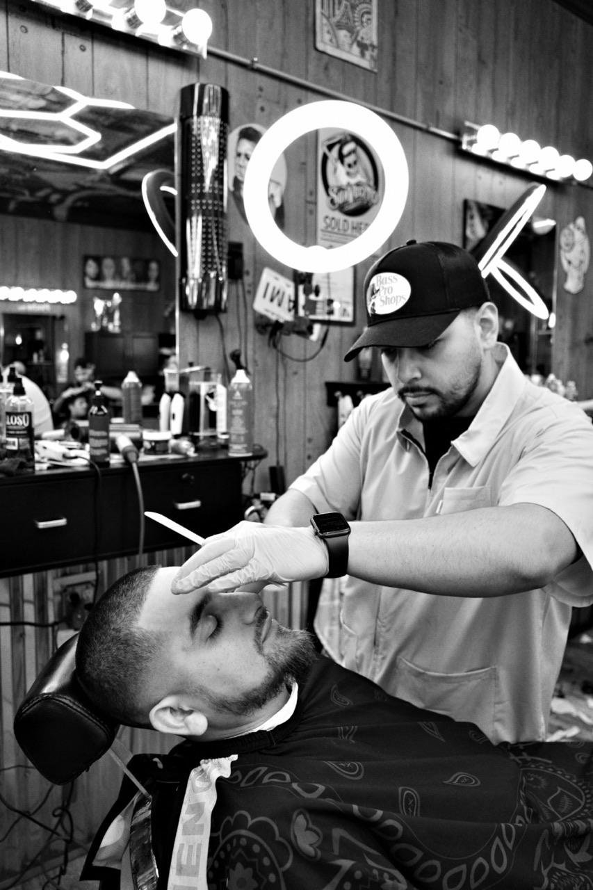 Owner of Fade Society mid-shave, gloved hand on a straight razor